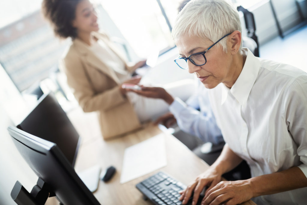 Woman in white collared shirt typing at a work computer